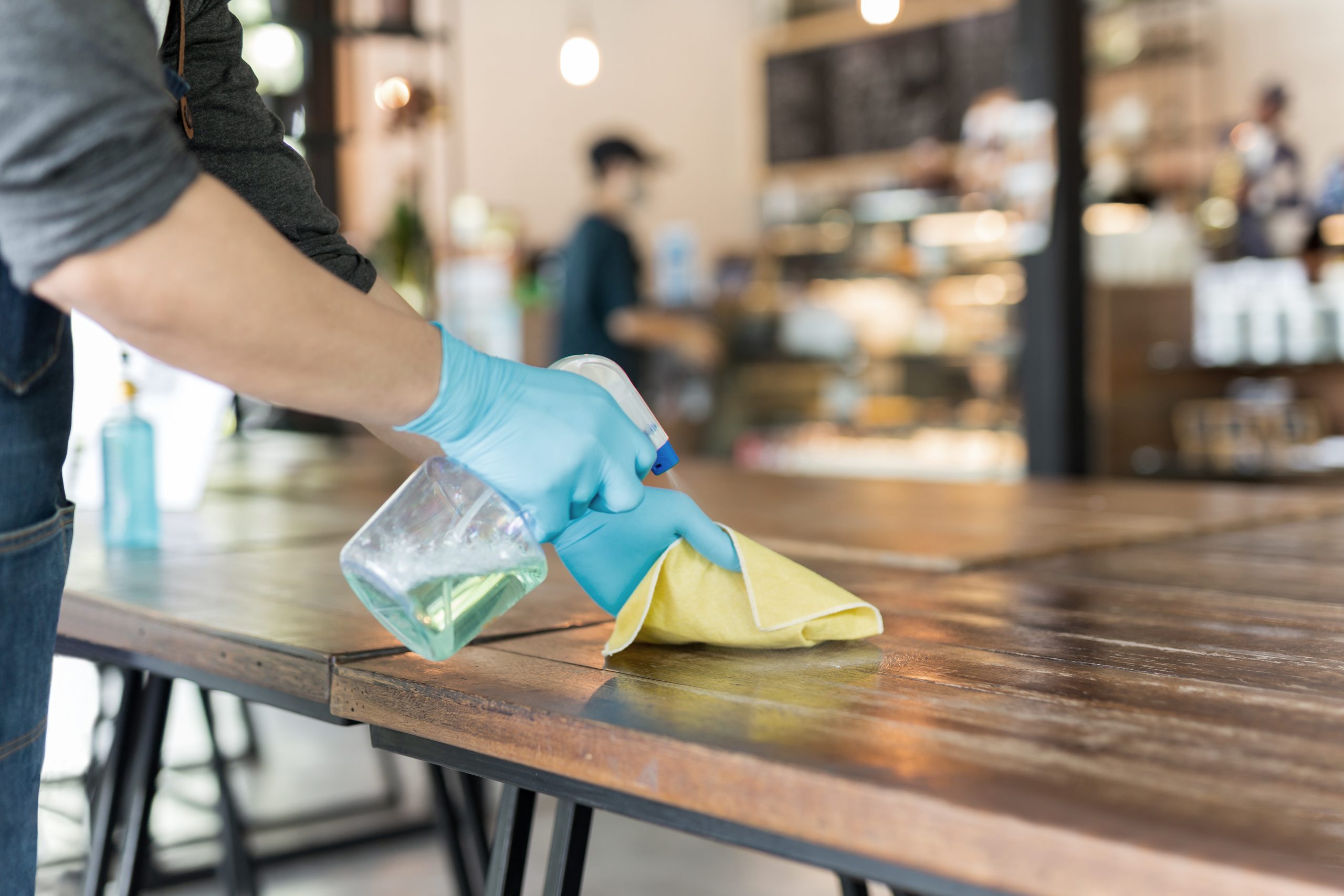 Waiter cleaning the table with disinfectant spray and microfiber cloth in cafe